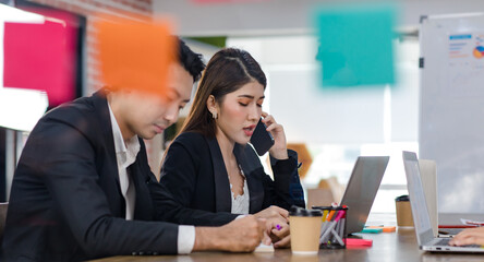 Asian young beautiful professional successful businesswoman in formal suit sitting smiling holding tablet pointing showing information data from laptop notebook computer to male businessman colleague