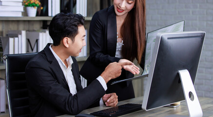 Millennial Asian young professional successful male businessman ceo entrepreneur in formal suit sitting looking reading checking paperwork document in folder from female businesswoman secretary