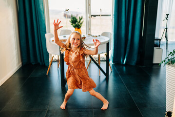 Funny adorable happy kid girl jump at home indoors, cute little child having fun dancing to music playing indoors alone enjoy pretending dancer in the morning