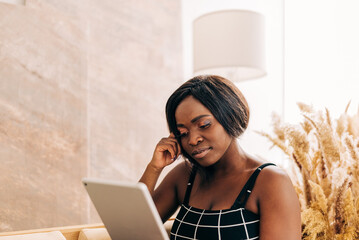 Beautiful young woman looking to the tablet sitting on the couch using technology. Online...