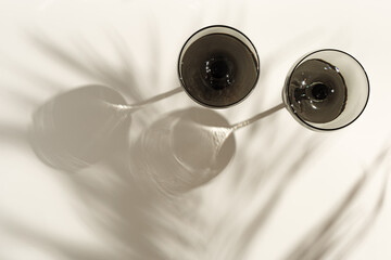 Champagne glasses tinted grey glass on beige background with palm leaf shadows from sunlight....