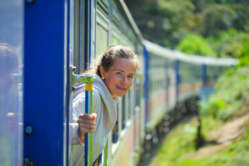 young woman peeks out from a train in the mountains of sri lanka