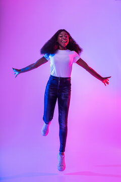 Full length of active happy millennial African American woman jumping in neon light. Positive emotions concept