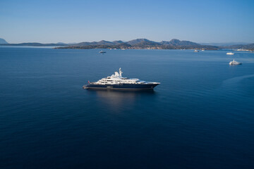 White blue mega yacht anchored off the coast of sardinia aerial view. One of the largest yachts on dark blue water in the background coastline, mountains, blue sky top view.