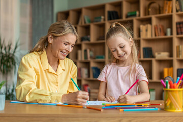 Creativity lessons for children. Happy girl drawing with professional female teacher at cabinet, enjoying art classes