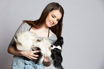 A cute young woman is hugging her papillon puppy. Love between owner and dog. Girl with dog studio portrait.