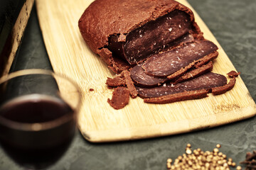 sliced basturma on a plate next to a bottle of wine and a glass