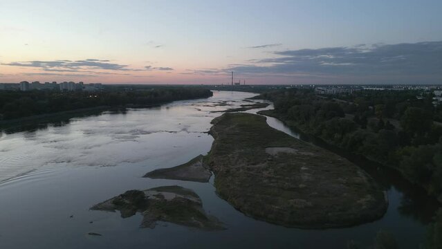 Drone shot of the wide riverbed of the Vistula River. In the distance, a panorama of residential houses and a coal-fired power plant