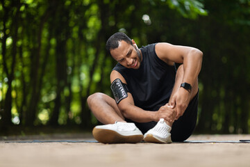 African american athlete in pain touching his ankle