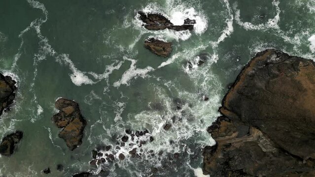 Aerial drone shot birds-eye view of waves crashing against the shore and rocks at the beach.