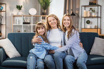 Portrait of happy mother hugging two little kids. Joyful affectionate mom cuddling sweet sibling daughters, looking at camera with toothy smile. Family relationship, motherhood. Head shot.