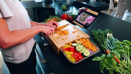 Cutting board with knife and a carrot with other vegetables and a tablet with recipes. Preparation of a vegan or vegetarian salad.