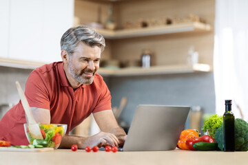 Cheerful grey-haired man cooking at home, reading food blog