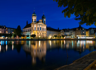 Fototapeta na wymiar Luzern, Switzerland, July 11, 2022: Night view of the Jesuit Church in Lucerne and its reflection in the Reuss River, Switzerland