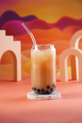 One glass with trendy asian drink iced boba bubble tea with tapioca pearls and milk with glass drinking straw on bright colorful red and orange background