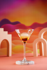 One martini glass with ice cube and brown alcoholic drink on bright colorful red and orange background