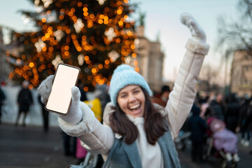 smiling happy woman at christmas city fair holding phone with white screen