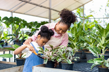 African mother is teaching her daughter to grow ornamental houseplant using trowel to put organics...