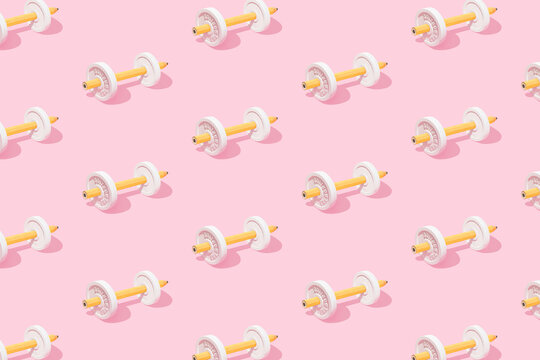 Yellow pencils and dumbbells on isolated pastel pink background. Minimal abstract pattern. Drawing or writing exercises. Back to school concept. Word energetic is reversed like a mirror reflection.