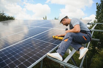 Male engineer in protective helmet installing solar photovoltaic panel system. Alternative energy ecological concept.