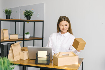 A cute girl is sitting in the office with a laptop and holding eco food packaging in her hands