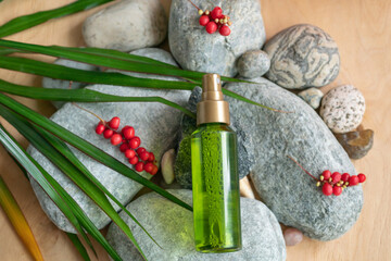 A bottle of green color with a spray bottle lies on the stones, next to the green leaves and berries of schisandra chinensis.Organic cosmetics.Schisandra chinensis cosmetic extract for spa