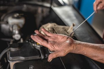 An old mechanic checks the transmission fluid of an old sedan with a dipstick.