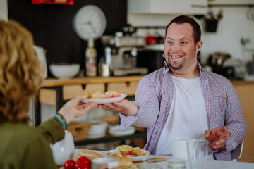 Portrait of happy young man with Down syndrome with his mother at home having breakfast together.