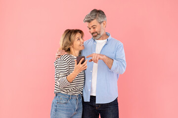 Middle Aged Married Couple Using Cellphone On Pink Studio Background