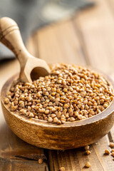 Uncooked buckwheat grain in bowl on wooden table.