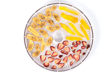 electric dryer for fruits and vegetables, close-up, strawberries, banana and mango are laid out on a round grate, on a white background