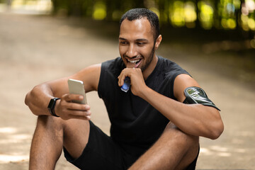 Positive black athlete having snack, resting after workout outdoors