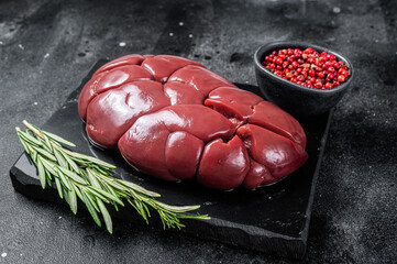 Beef veal kidney, raw offal meat on marble board with rosemary. Black background. Top view