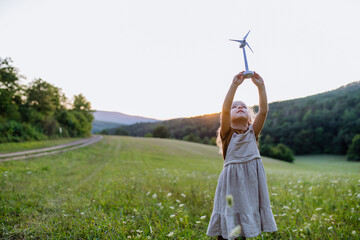 Little girl standing in nature with model of wind turbine. Concept of ecology future and renewable...