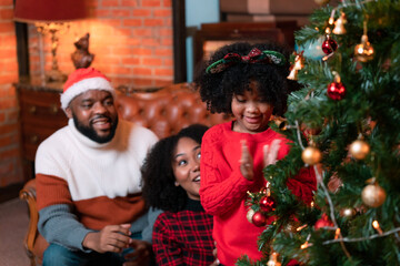 Family, father, mother and children are rejoicing in decorating the Christmas tree in the house.