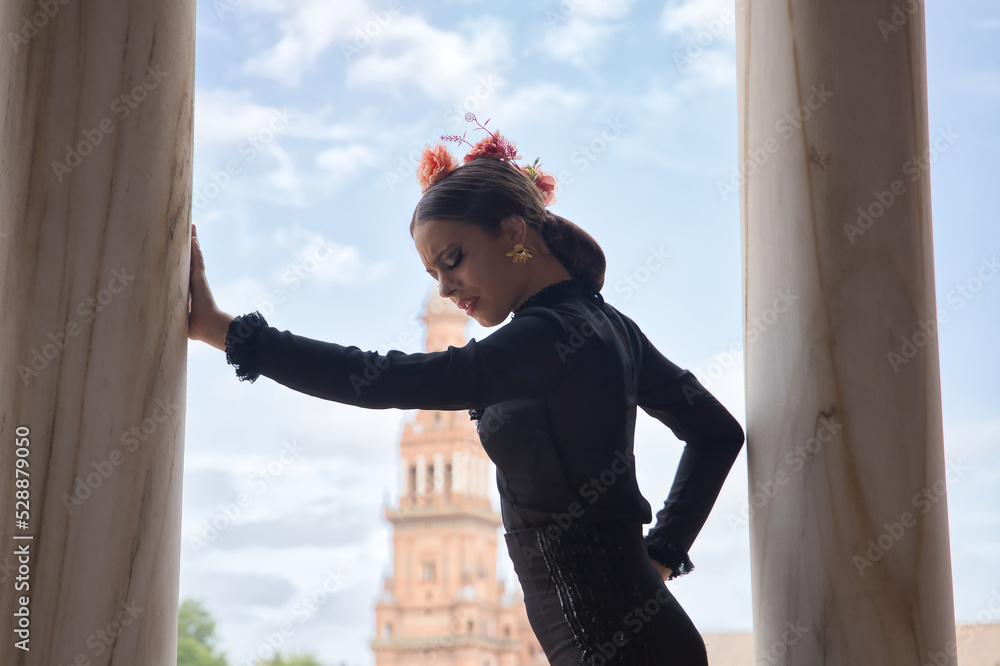 Canvas Prints Young teenage woman with black dance dress and pink carnations in her hair, doing flamenco pose leaning on a column. Flamenco concept, dance, art, typical Spanish dance.