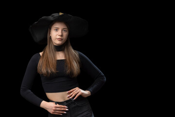 Portrait of girl in black short top, jeans and wide-brimmed hat in the studio. Copy space, mockup. Black background.