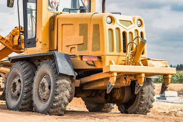 Road grader at the construction site. Powerful construction machine for ground leveling and excavation. Close-up. Professional construction equipment.