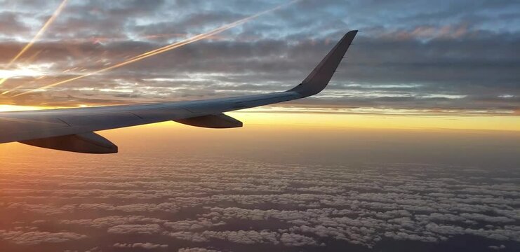 View of fantastic sunrise with reddish and orange colors among the clouds from the window of the seat overlooking the wing of the plane