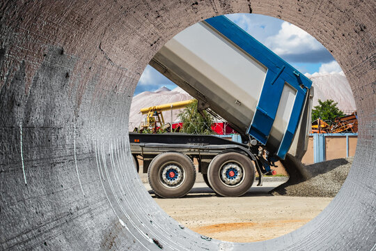 A large dump truck unloads rubble or gravel at a construction site. Car tonar for transportation of heavy bulk cargo. Providing the construction site with materials. View from a large concrete pipe.