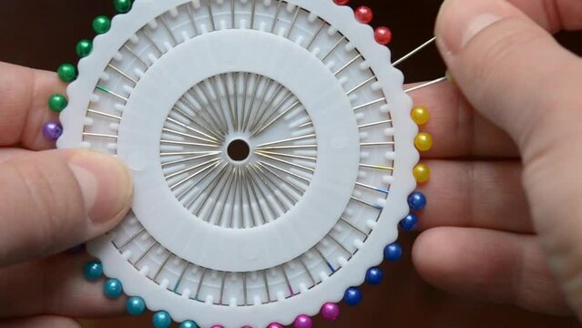 A seamstress woman pulls out and removes a pin with plastic head from a set of white discs. Dressmaker get a multi-colored needle and put it back