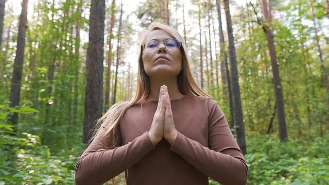 Young positive woman meditating, inhaling fresh wood nature air, taking deep breath for oxygen, reducing stress, leaving bad thoughts and enjoying silence and healthy lifestyle in a forest park.