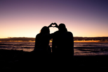couple making a heart with their hands in a sunset on the beach