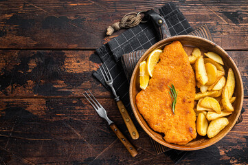 Austrian fried weiner schnitzel with potato wedges in a wooden plate. Wooden background. Top view. Copy space - obrazy, fototapety, plakaty