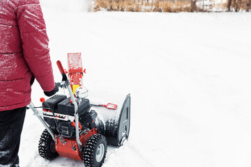 Detail of portable red snow blower powered by gasoline in action. Man outdoor using snowblower machine after snowstorm. Snow removal, thrower assistant in winter. Guy blowing snow during blizzard