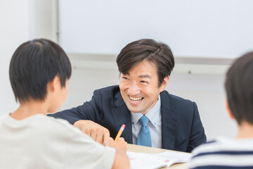 小学生に勉強を教える笑顔の塾講師・先生（日本人男性）
