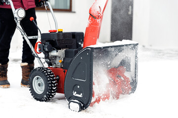 Closeup of red snow blower in action. Senior mature man outdoor in front of house using snowblower machine for removing snow on yard. Snow thrower in winter outside home. Young worker guy blowing snow