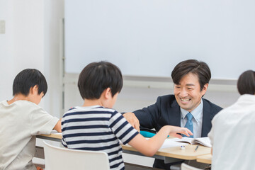 小学生に勉強を教える笑顔の塾講師・先生（日本人男性）
