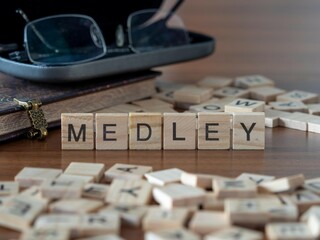 medley word or concept represented by wooden letter tiles on a wooden table with glasses and a book