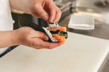 Chef hands cooking sushi with rice, salmon and nori on kitchen of japanese restaurant